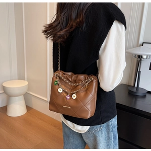 Detail of brown quilted bucket bag with chain strap and colorful enamel heart charms
