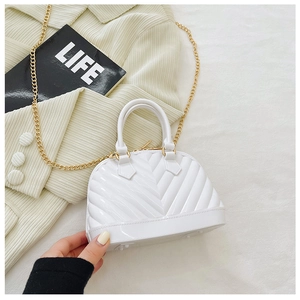 Detail of white glossy jelly shell bag with elegant gold metal chain strap on textured fabric
