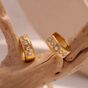 Macro shot of 18K gold-plated twisted earrings with clear rhinestones on a wooden branch