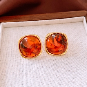 Detail view of amber resin square earrings with gold metal frame on a linen tray