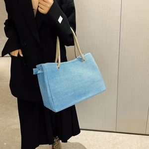 Light blue woven tote bag with rope handles worn by a model in a black suit