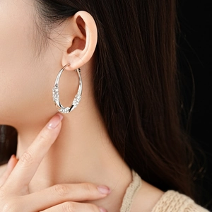 Close-up of twisted silver hoop earrings with clear rhinestones worn by a model