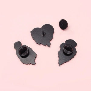 Black enamel skull heart wing brooches set with rubber clutch back on pink background