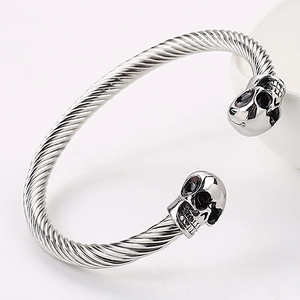 Detailed view of silver skull charms and twisted wire cable on a C-shaped open cuff bracelet