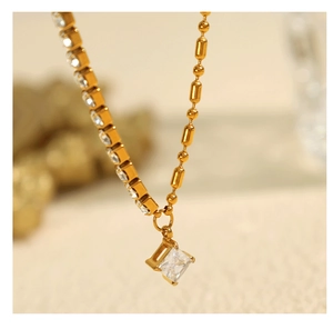Détail d'un collier doré avec pendentif carré en cristal et chaîne rivière scintillante