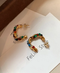 Detail of gold twisted C-shaped earrings with colorful stone beads and silicone plugs