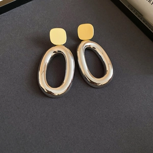 Detailed view of geometric mixed-metal earrings with gold square studs and silver oval rings