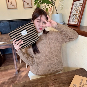 Detail of plush black and brown striped cosmetic bag held in a cozy cafe setting