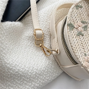 Round woven straw crossbody bag with floral embroidery and adjustable leather strap