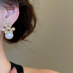 Close-up of rose gold clover earrings with micro-pave crystals and a large white pearl