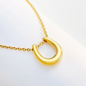 Polished gold horseshoe U-shape pendant necklace with delicate chain on white background