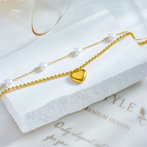 Double-layered golden beach anklet with heart pendant and pearl details on stone surface