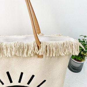 Detailed close-up of woven canvas tote featuring black sun print and decorative fringe tassels