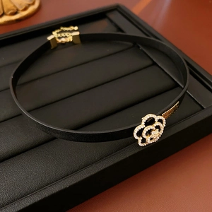Detail of leather choker featuring a gold flower clasp with pearl and brand tag