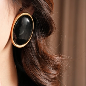 Close-up of vintage oval black resin earrings with a minimalist gold metal frame on model