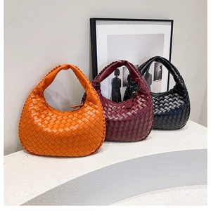 Detail of three leather woven hobo bags in orange, burgundy, and black on stone steps