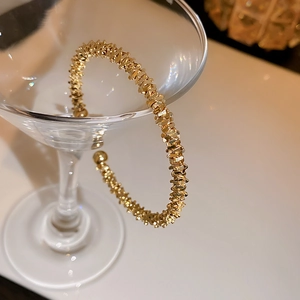 Detail of gold geometric textured open cuff bracelet hanging on a cocktail glass rim