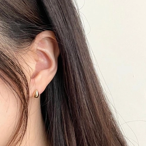 Close-up of a minimalist golden water drop earring worn on a female model's ear