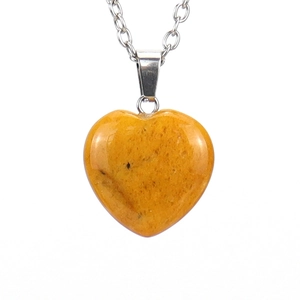 Detail of yellow natural stone heart pendant with silver chain on white background