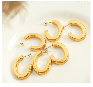 Detailed view of three pairs of minimalist C-shaped polished gold-plated earrings on ceramic