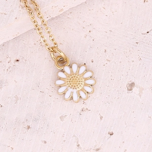 Macro shot of gold daisy pendant with white enamel petals on a textured stone surface