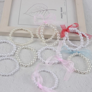 Children's faux pearl bracelets with colorful ribbon bows on a neutral background
