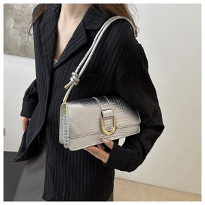 Detail of silver crocodile-embossed handbag with gold horseshoe buckle and knotted strap