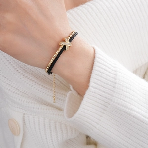 Close-up of gold double-layer chain and black cord bracelet with pavé crisscross detail