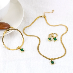 Conjunto de joyas doradas con gemas verdes rectangulares sobre tela blanca texturizada