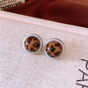 Détail de boucles d'oreilles rondes motif léopard avec bordure blanche et résine