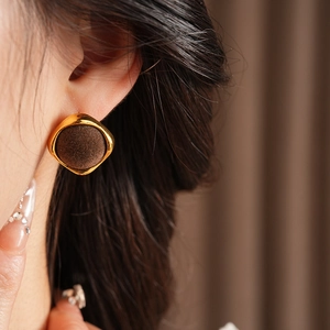 Gros plan de boucles d'oreilles carrées marron avec bordure dorée portées par un mannequin