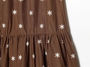 Makrodetail aus dunkelbraunem Stoff mit weißer Stickerei und gefaltetem Rüschensaum