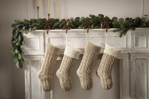 Detail of knitted Christmas stockings in beige and white hanging on a fireplace mantel