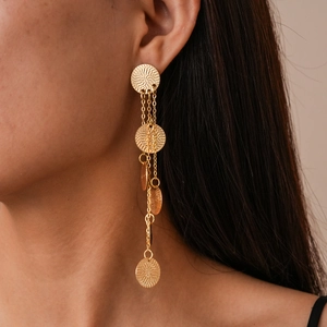Detail of long gold tassel earrings with textured circular metal discs on model