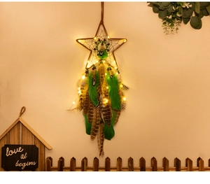 Star-shaped dream catcher with green feathers and LED fairy lights hanging on warm wall