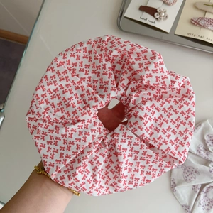 Detail of oversized white cotton scrunchie with cute red bow print held in hand
