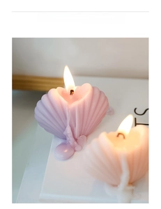 Macro shot of seashell-shaped candles in pink and purple gradients with warm burning flame