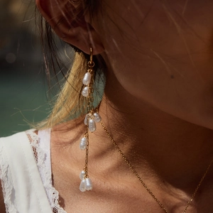 Detail of elegant gold tassel earrings with baroque pearls worn by a model in soft light