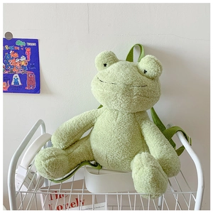 Detail of cute green frog plush backpack on a white shelf with soft texture and straps