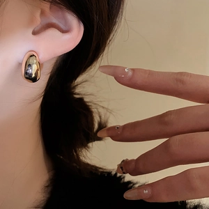 Close-up of a model wearing minimalist golden teardrop earrings with a polished metal finish