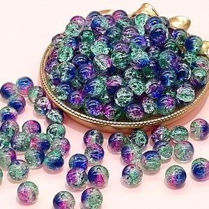 Macro shot of 10mm blue-purple and green crackle glass beads on a gold tray for DIY jewelry