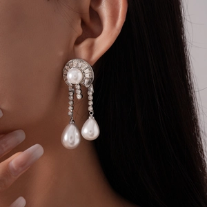 Close-up of geometric silver drop earrings with layered pearls and sparkling diamond accents