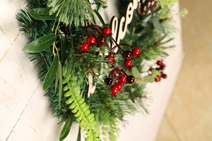 Detail of Christmas wreath with pine needles, red berries and wood Welcome sign