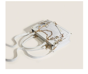 Close-up of white quilted tote bag featuring golden butterfly charms and chain detail