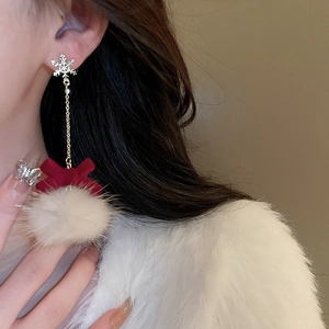 Close-up of red velvet bow earrings with snowflake studs and white fur pom-poms