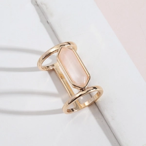 Golden double-band ring featuring a hexagonal translucent pink crystal on a marble surface