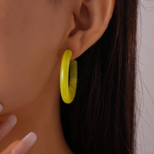 Close-up of a vibrant yellow resin C-shaped hoop earring worn on a model's ear