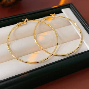 Détail de grandes créoles plaquées or avec texture facettée dans une boîte à bijoux
