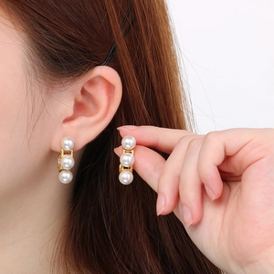 Detailed macro view of triple white pearls set on vertical 18k gold-plated C-shape earrings