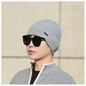 Detailed close-up of light gray knit beanie with metal logo tag and ribbed texture